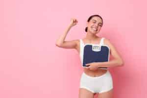 Woman holding a scale with other arm in the air celebrating her weight loss because of GLP-1 Agonists in Austin, TX